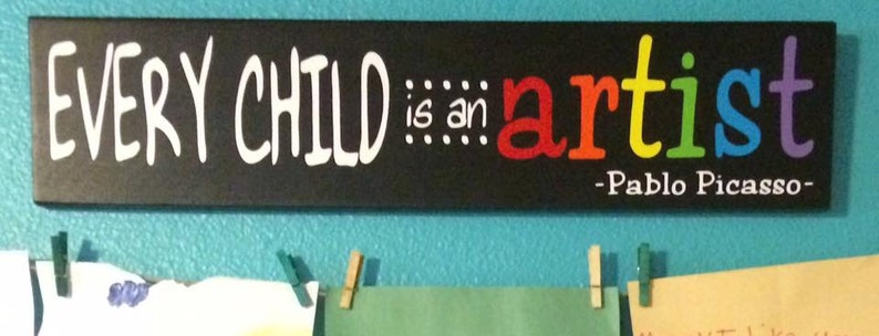 May include: Black chalkboard sign with the text "EVERY CHILD is an artist" in white lettering. The word "artist" is written in rainbow colors. The quote is attributed to Pablo Picasso.