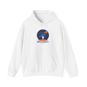 Könnte beinhalten: Weißer Kapuzenpullover mit Fronttasche und Kordelzug. Auf der Vorderseite befindet sich eine runde Grafik einer Person auf einem Planeten, mit Sternenhimmel und dem Text "ORBITAL MINDSET".