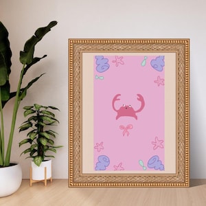 May include: A framed print with a pink background, featuring a cartoon crab, bows, starfish, and shells. The frame is gold-coloured. The artwork has a sea theme.