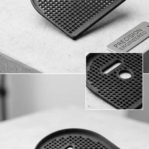 Op de afbeelding: Een zwart, 3D-geprint onderdeel met een gaaspatroon en een gebogen vorm. Het onderdeel heeft een rechthoekige uitsparing en een cirkelvormig gat. De tekst "HIGH-QUALITY 3D PRINT" is zichtbaar. Een klein metalen label leest "PRECISION ENGINEERED".