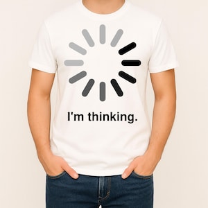May include: A white short-sleeved t-shirt featuring a circular loading icon composed of twelve grey and black segments arranged in a radial pattern. Below the graphic, the text "I'm thinking." is printed in a simple, black sans-serif font.