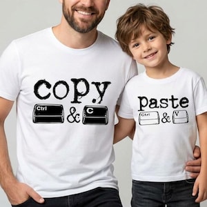 May include: Two white short-sleeved t-shirts. The larger shirt features the black text copy and keyboard keys labelled Ctrl and C. The smaller shirt features the black text paste and keyboard keys labelled Ctrl and V. Both shirts have a crew neckline.