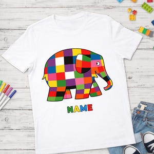 May include: White t-shirt with a vibrant, chequered elephant illustration. The elephant is made up of squares in red, yellow, green, blue, purple, and orange. The word "NAME" is printed in green, yellow, red, and blue.