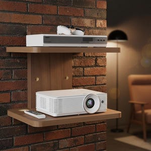 May include: A home theater setup featuring a white projector and a media player on a wooden shelf. The shelf is mounted on a brick wall. A remote control sits on the shelf. Sunglasses rest on top of the media player.