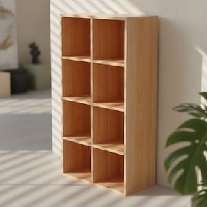 May include: A tall, rectangular wooden shelving unit featuring a light brown wood grain finish. The structure is divided into eight equal, open square compartments arranged in two vertical columns of four, providing ample storage space for various items.
