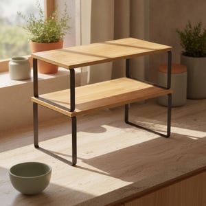 May include: A two-tier countertop shelf featuring two rectangular light brown bamboo wood surfaces supported by a black metal frame. The structure consists of two U-shaped metal legs on each side that connect the top and bottom wooden shelves.