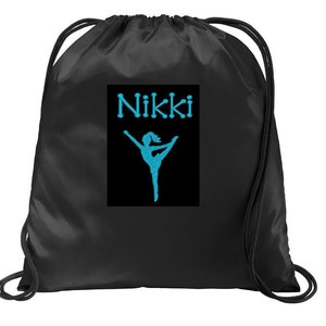Op de afbeelding: Zwarte trekkoordtas met een turquoise geborduurd ontwerp. Het ontwerp toont de naam "Nikki" boven een silhouet van een persoon in een balletpose. De tas heeft zwarte trekkoorden.