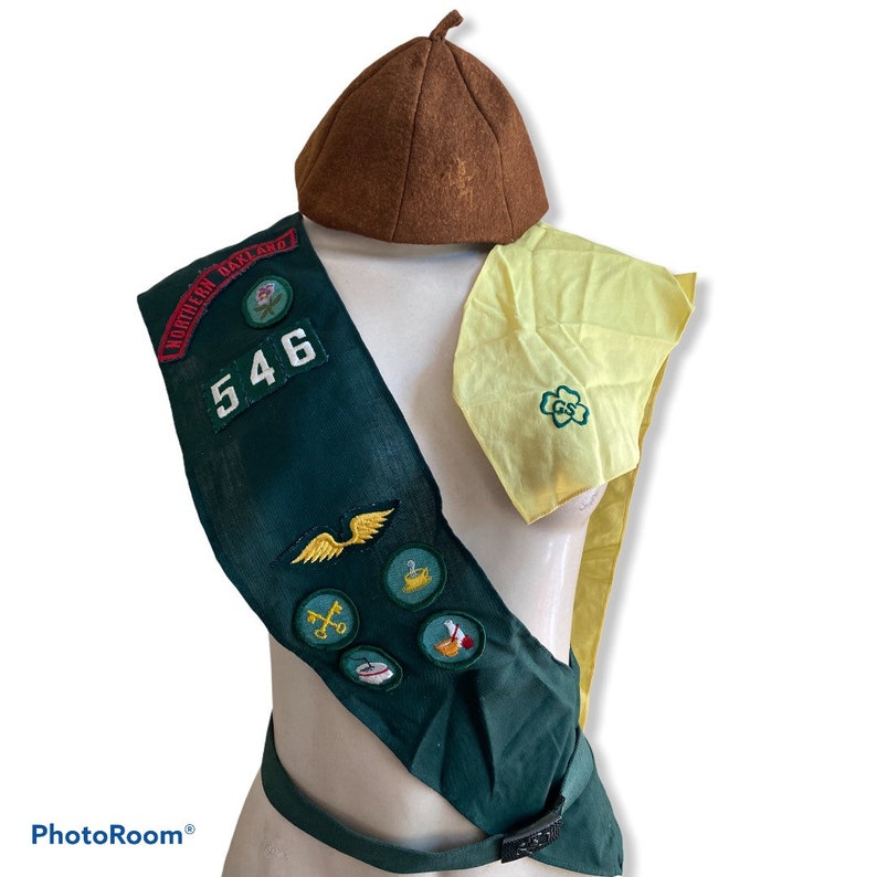 Puede incluir: Una banda verde de Girl Scout con un sombrero de fieltro marr&oacute;n, un pa&ntilde;uelo amarillo y varias insignias. La banda tiene el texto "Northern Oakland" y el n&uacute;mero "546".