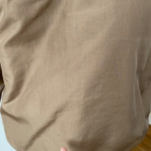 Pode incluir: Uma jaqueta bege com um acabamento liso e ligeiramente brilhante. A jaqueta tem um fecho de correr e uma gola alta.