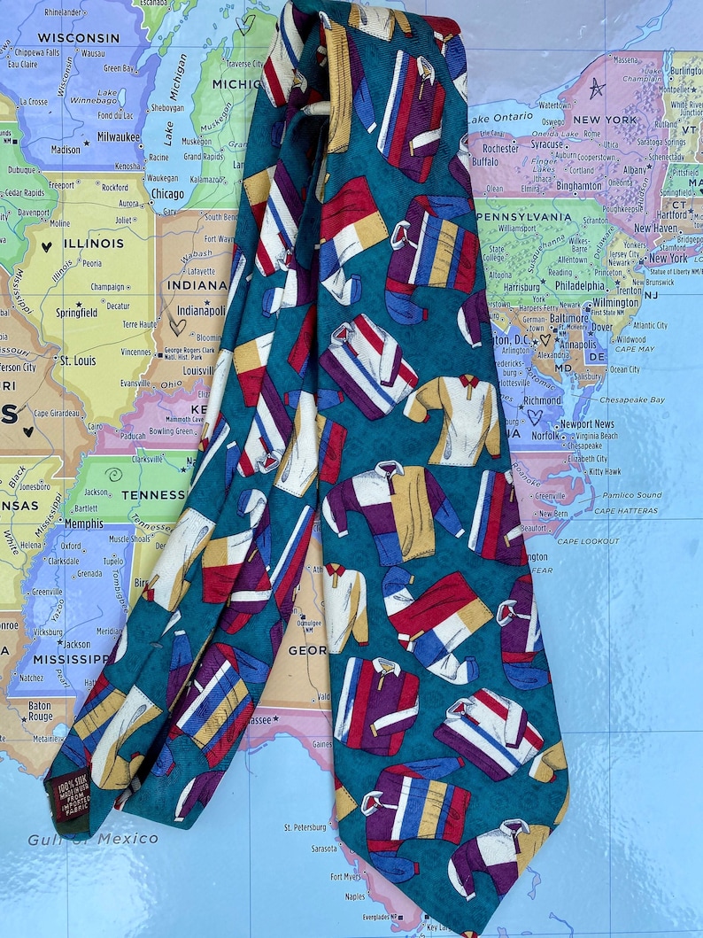 May include: A teal blue silk tie with a repeating pattern of colorful athletic jerseys. The jerseys are in various colors, including red, white, blue, yellow, and purple.