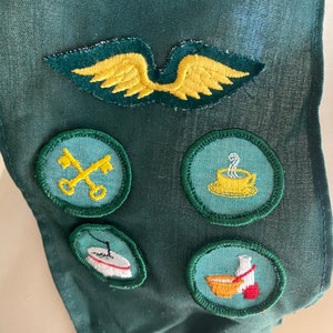 Puede incluir: Una faja de tela verde con cinco parches bordados. Los parches son amarillos, verdes y blancos con varios dise&ntilde;os, incluyendo una llave, una taza de caf&eacute;, una aguja de coser y un taz&oacute;n de sopa.