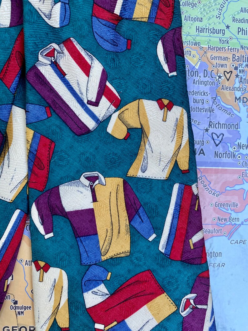 May include: A teal blue silk tie with a repeating pattern of colorful polo shirts. The tie is partially obscured by a map of the eastern United States.