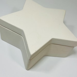May include: A cream-coloured star-shaped box with a lid. The box is made of a solid material and has a matte finish. The lid fits snugly on top of the box, creating a clean, seamless look. The box is designed to hold small items.