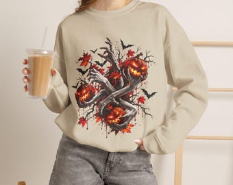 May include: A beige crewneck sweatshirt featuring a graphic print of three glowing jack-o'-lanterns held by skeletal hands, surrounded by black bats, bare tree branches, and red autumn maple leaves, creating a detailed seasonal illustration.