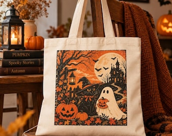 May include: A cream-colored canvas tote bag featuring a square graphic print of a black cat wearing a witch hat, a ghost holding a small pumpkin, jack-o'-lanterns, a haunted house, bats, and a full moon against an orange autumn forest background.