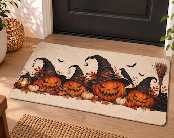 May include: A rectangular doormat with a beige background featuring a printed design of four orange jack-o'-lanterns wearing black witch hats, surrounded by autumn leaves, a lantern, a black crow, a broom, and a black cat.