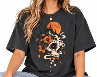 May include: A charcoal gray short-sleeve t-shirt featuring a graphic print of a human skull adorned with orange lilies, a winding path leading to a dark castle silhouette, and a large orange moon in the background with swirling smoke accents.