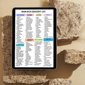 May include: A digital tablet displays an "Iron Rich Grocery List" with categories like leafy greens, pulses, animal proteins, and fruits. The list includes various food items, such as spinach, lentils, beef, and dates. The tablet rests on a textured stone surface.