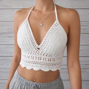 Puede incluir: Top halter de ganchillo blanco con cuello en V. El top presenta un dobladillo festoneado y un diseño calado. Las correas son finas. La prenda está hecha de hilo suave y texturizado. Hecho a mano.