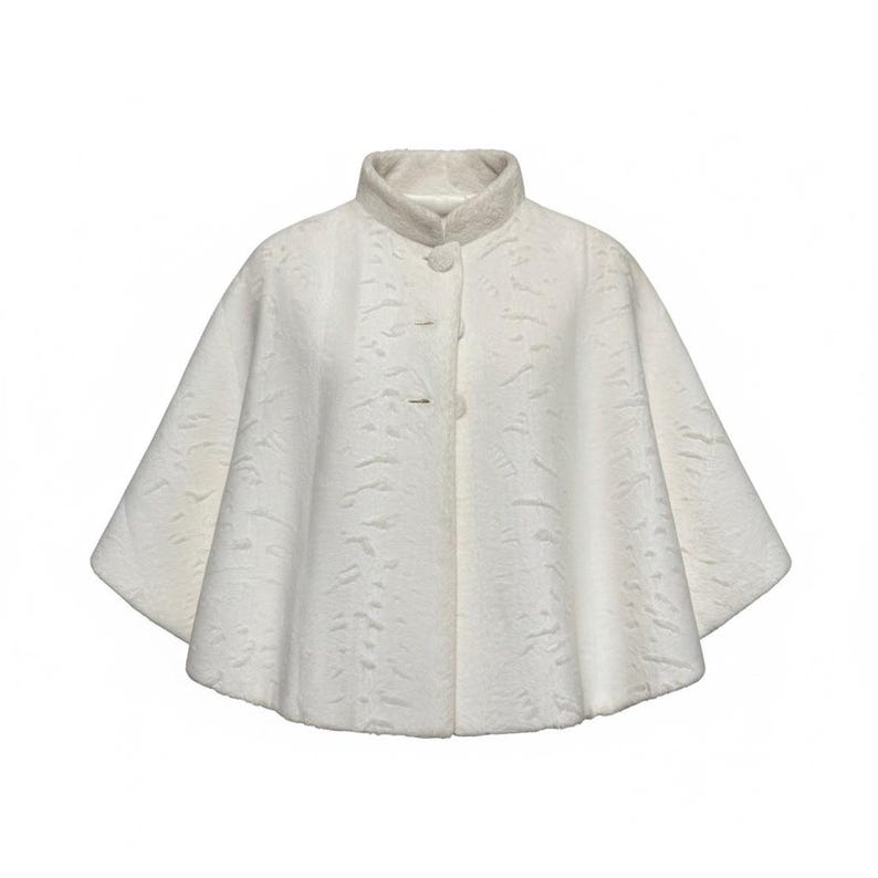 May include: A white cape with a textured surface and a high collar. The garment features a flared silhouette and is fastened at the front with three matching circular buttons. The fabric has a subtle, wavy pattern throughout the entire piece.