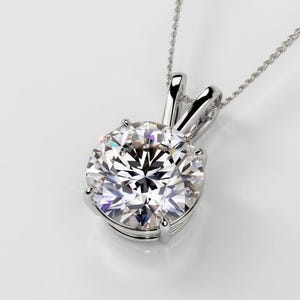 Puede incluir: Un collar con colgante de diamantes de talla redonda. El diamante está engastado en una montura de plata y cuelga de una delicada cadena de plata. El diamante brilla con muchas facetas.