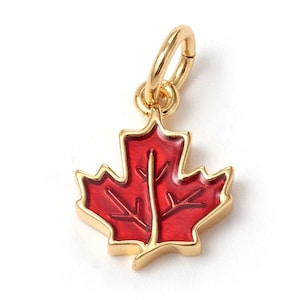 May include: A gold-colored charm in the shape of a red maple leaf. The charm has a loop at the top for attaching to a bracelet or necklace.
