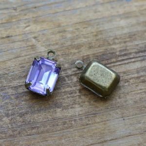 May include: Two metal settings for a pendant, one with a clear purple glass stone and the other empty.