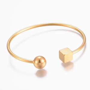 May include: A gold-toned bangle bracelet with a round ball on one end and a square charm on the other.