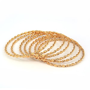 May include: A set of six gold-toned bangle bracelets with a twisted design. The bracelets are stacked on top of each other.