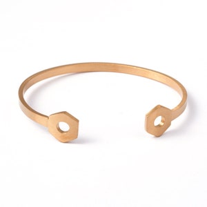 May include: A gold-toned metal bracelet with hexagonal end pieces. The bracelet is open and ready to be worn.