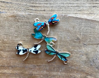 May include: Four dragonfly charms with different colored wings. The charms are made of metal and have a gold finish. The wings are decorated with a variety of patterns, including blue, green, red, white, and black.