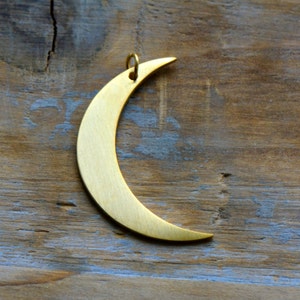 May include: A gold crescent moon pendant charm. The charm is made of metal and has a smooth, polished finish.