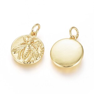 May include: Two gold-toned metal charms, one featuring a detailed bee design and the other plain. Both charms are round and have a loop for attaching to a necklace or bracelet.