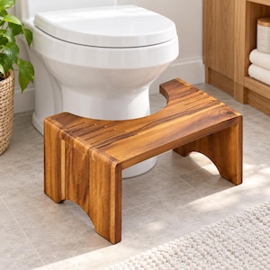 May include: A brown wooden toilet stool with a curved cutout design, featuring a natural wood grain finish and grooved traction lines on the top surface. The stool has four sturdy legs and is positioned in front of a white porcelain toilet.
