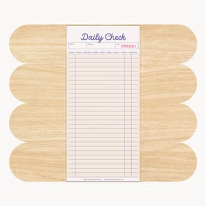 May include: A notepad with the words "Daily Check" in a script font at the top. The notepad has a grid of lines and boxes for writing. The notepad is on a light brown, scalloped wooden base.