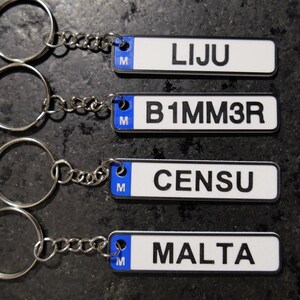 May include: Four keyrings with white rectangular tags and black text. The tags have a blue border and the letter "M". The text on the tags reads: "LIJU", "B1MM3R", "CENSU", and "MALTA". Each keyring has a silver ring and chain.