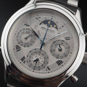 Puede incluir: Un reloj de pulsera analógico plateado con esfera blanca texturizada, números romanos y varias subesferas. La esfera presenta un indicador de fase lunar, un calendario y el texto SHELLMAN & CO. GRAND COMPLICATION impreso en color negro.
