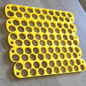 May include: Four bright yellow, slotted trays with multiple circular openings. The trays are arranged in a stack, with a hexagonal shape at each end. The trays are made of a solid material and are placed on a wooden surface.