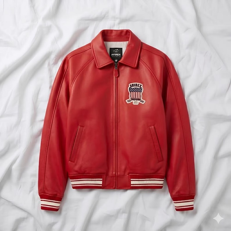 Peut inclure: Veste en cuir rouge vif avec un col classique et une fermeture &eacute;clair. Elle est orn&eacute;e d'un &eacute;cusson au design patriotique et du nom de la marque. Les poignets et l'ourlet sont orn&eacute;s de rayures blanches et rouges. La veste est pr&eacute;sent&eacute;e sur fond blanc.