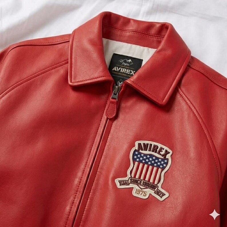 Peut inclure: Veste en cuir rouge avec un col et une fermeture &eacute;clair. La veste pr&eacute;sente un &eacute;cusson sur la poitrine avec la marque "AVIREX" et un motif de drapeau am&eacute;ricain. La veste a un style classique et vintage.