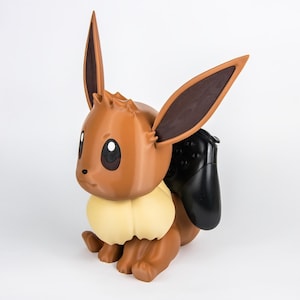 May include: A brown Eevee figure with large ears and a cream-colored ruff. A black game controller is attached to its back. The figure is a collectible item.