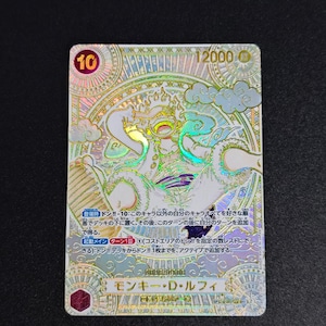 以下が含まれることがあります： キャラクターイラストが描かれた、日本語のテキストが入ったホログラフィックトレーディングカード。 カードは金と銀の配色で、円の中に数字の「10」が入っています。 キャラクターは、詳細な背景とともに、ダイナミックなポーズで描かれています。