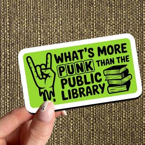 May include: A rectangular sticker with a lime green background and white border. The sticker features black text that reads "WHAT'S MORE PUNK THAN THE PUBLIC LIBRARY" and a graphic of a hand making a rock and roll gesture, and a stack of books.