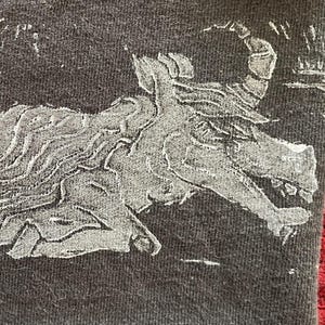 May include: Dark gray fabric with a detailed, white illustration of a mythical creature. The creature has a horned head, a long body, and a curled tail. The design appears to be embossed or printed on the fabric.