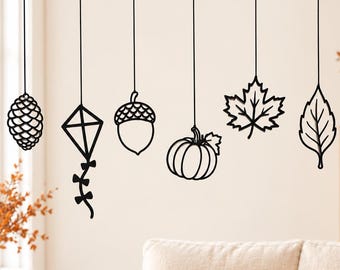 May include: A set of six black hanging ornaments suspended from a horizontal branch, featuring a pinecone, a kite, an acorn, a pumpkin, a maple leaf, and a pointed leaf. Each ornament is crafted from a thin, flat material with a cutout design.