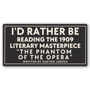 May include: A black rectangular sticker with a white border. The text on the sticker reads "I'D RATHER BE READING THE 1909 LITERARY MASTERPIECE 'THE PHANTOM OF THE OPERA' WRITTEN BY GASTON LEROUX."