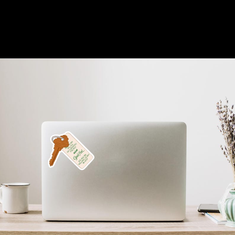 May include: A sticker featuring a vintage hotel key and tag. The key is brown, and the tag is cream-colored with green text that reads "Good Hotel" and other phrases. The sticker is placed on a white laptop.