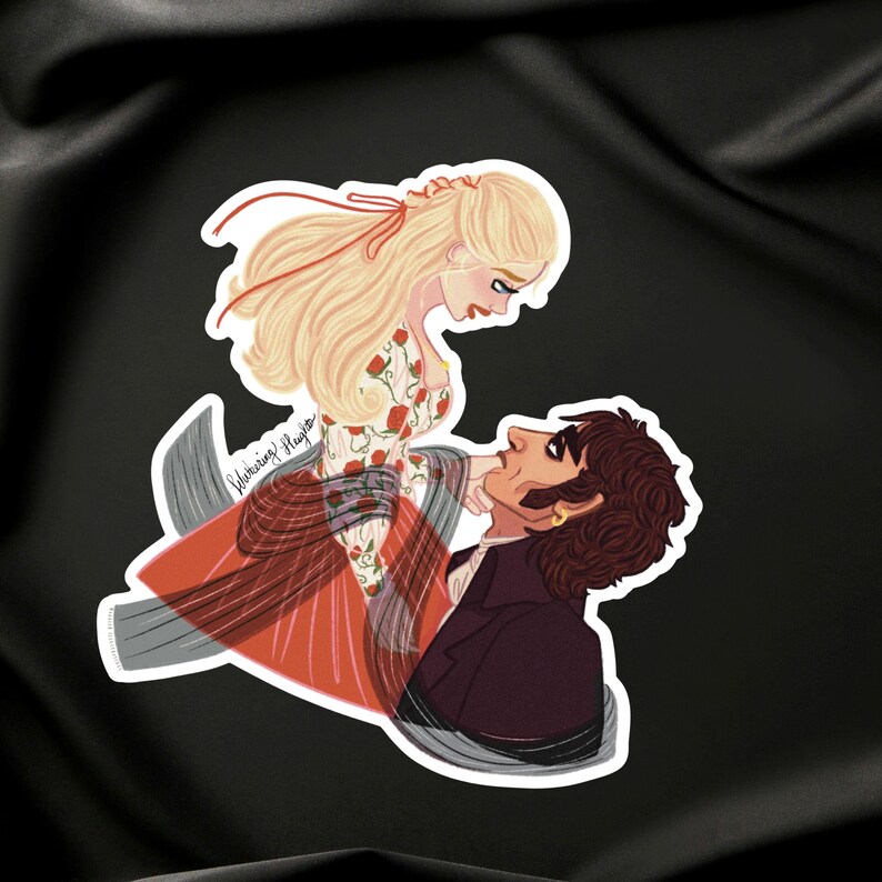 May include: A sticker featuring a romantic illustration of a man and woman. The woman has long blonde hair and wears a dress with red floral patterns. The man has dark hair and a dark coat. The sticker has a white border.