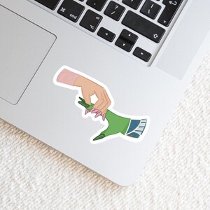 May include: A sticker featuring a green hand with blue denim and a pink hand with pink nails, both hands are reaching out to each other.