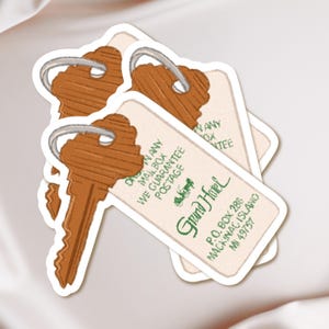May include: A stack of stickers featuring vintage-style hotel key tags. The tags are cream-colored with brown keys and green text that reads "Grand Hotel, Mackinac Island, MI 49757". The tags also include the text "We Guarantee Postage".
